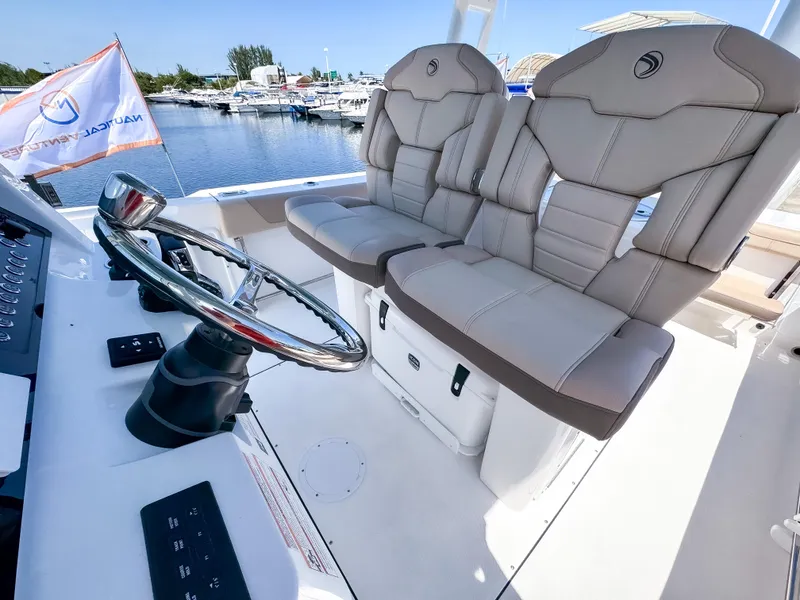 Slide: The Image of 2025 Edgewater 325CC boat interior with dual captain's chairs and steering wheel, docked by the water. - 9