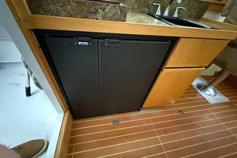 Slide: The Image of Compact kitchen area in 2013 Eco-Trawler 33 with fridge, sink, and wooden cabinetry. - 33