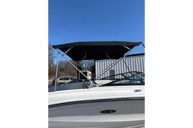 Slide: The Image of 2023 Sea Ray SPX 210 Outboard with black bimini top, parked outdoors. - 10