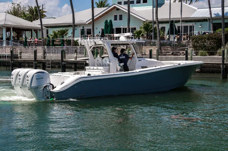 Slide: The Image of 2025 Edgewater 370CC boat cruising near a waterfront restaurant. - 5