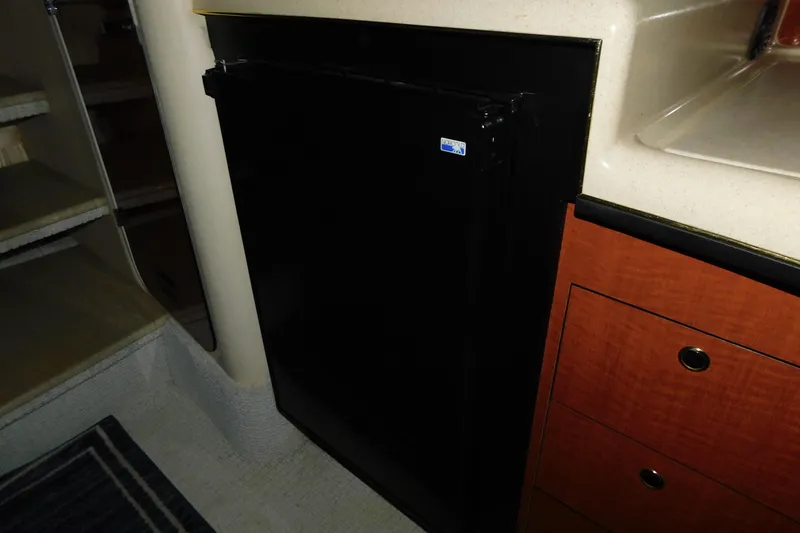 Slide: The Image of 2002 Sea Ray 340 Sundancer interior with black refrigerator and wooden cabinetry. - 25