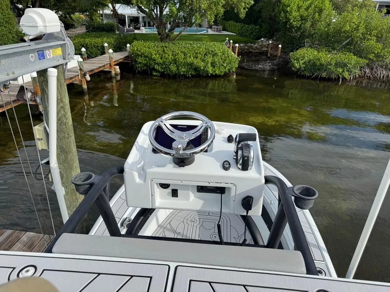 Slide: The Image of 2021 Yellowfin 26 Hybrid boat helm with steering wheel and controls, docked by lush greenery. - 28
