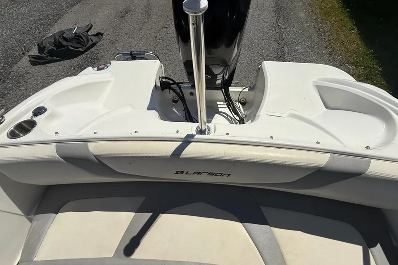 Slide: The Image of 2014 Larson LX 160S OB boat interior with seating and motor, parked on pavement. - 16