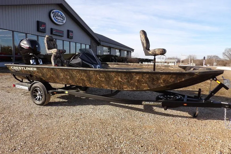 The Image of 2026 Crestliner XF 189 boat with camouflage design on a trailer outside a marine center. - 1