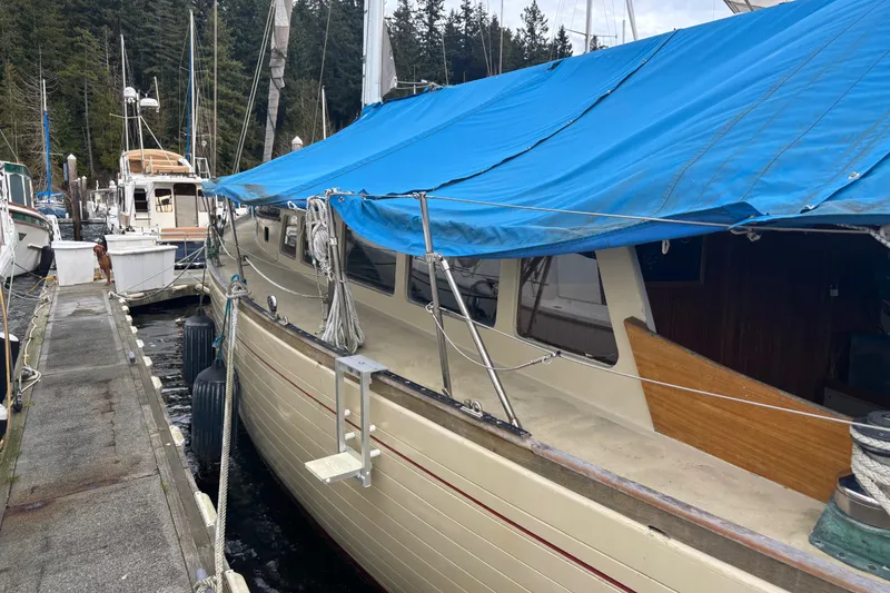 Slide: The Image of 1962 Kettenburg Sloop docked, covered with blue tarp, surrounded by other boats. - 2