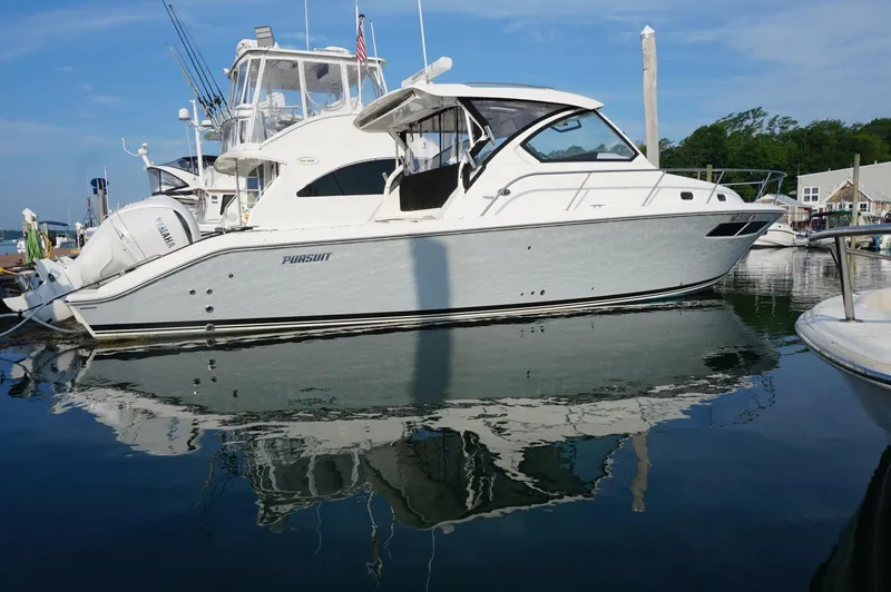 The Image of 2023 Pursuit OS 355 Offshore boat docked in a marina, reflecting on calm water. - 2