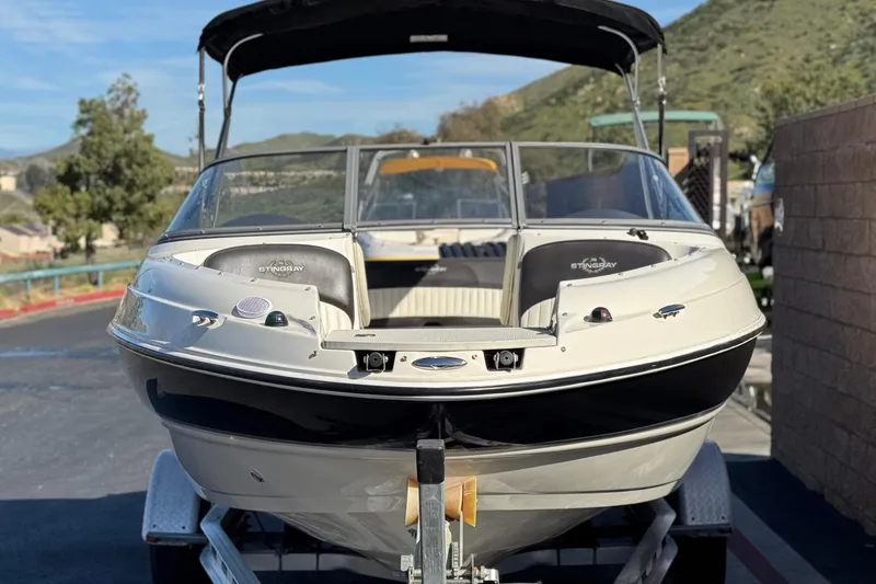 Slide: The Image of 2018 Stingray 208 LS boat on trailer, parked outdoors with scenic background. - 2