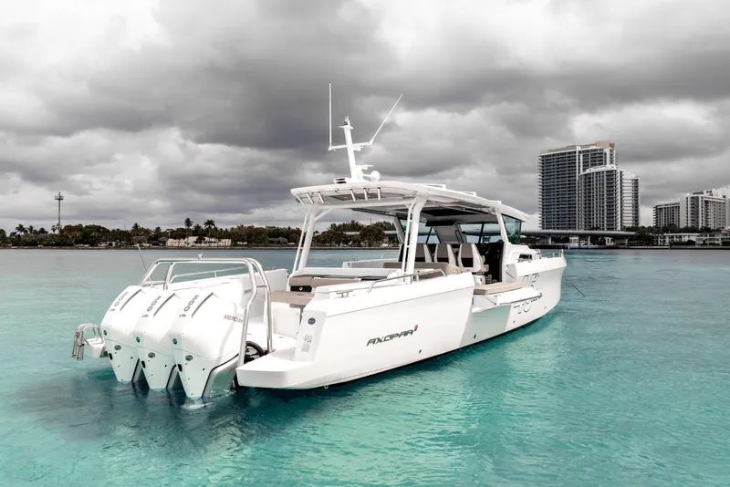 Slide: The Image of 2025 Axopar 45 Cross Top boat on turquoise water with cloudy sky backdrop. - 14
