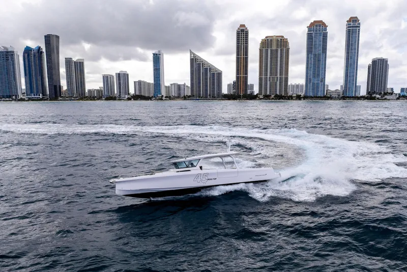 Slide: The Image of 2025 Axopar 45 Cross Top boat cruising near city skyline on a cloudy day. - 43