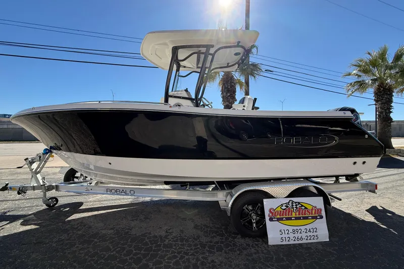 The Image of 2024 Robalo R230 Center Console boat on trailer, sunny day, palm trees in background. - 0