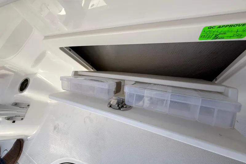 Slide: The Image of 2024 Robalo R230 Center Console storage compartment with tackle boxes and QC approval sticker. - 43