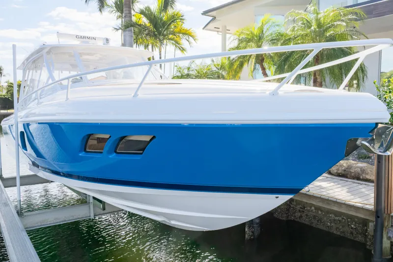 Slide: The Image of 2019 Intrepid 407 Cuddy boat with blue hull, docked near palm trees. - 16