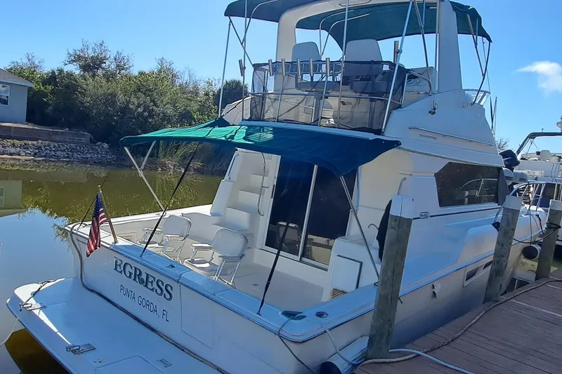 Slide: The Image of 2000 Silverton 42 Convertible yacht docked, featuring a blue canopy and American flag. - 2