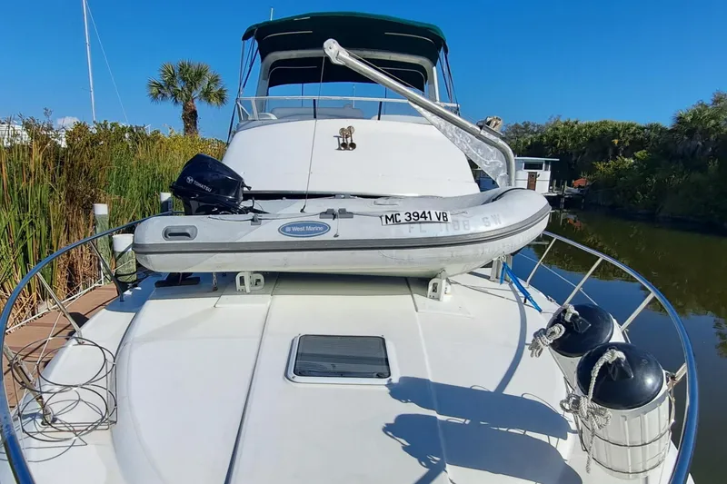 Slide: The Image of 2000 Silverton 42 Convertible yacht with inflatable boat on deck, docked near lush greenery. - 5