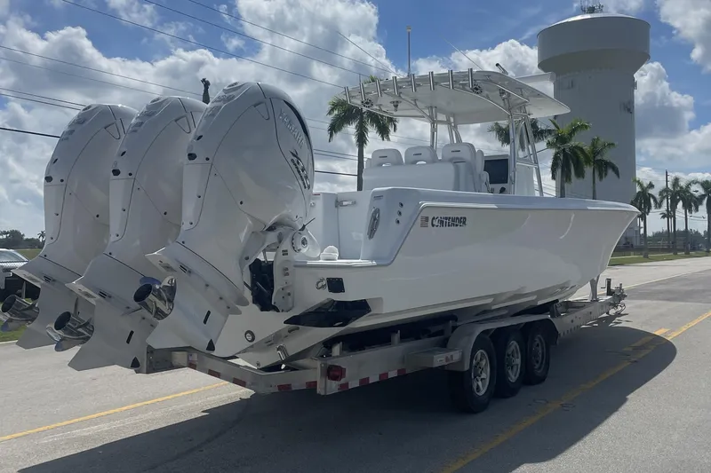 Slide: The Image of 2024 Contender 39 ST boat on trailer with triple outboard engines, palm trees in background. - 2