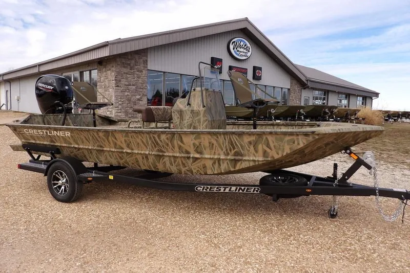 The Image of 2026 Crestliner 1870 Retriever FCC boat with camouflage design on a trailer outside a marine center. - 1