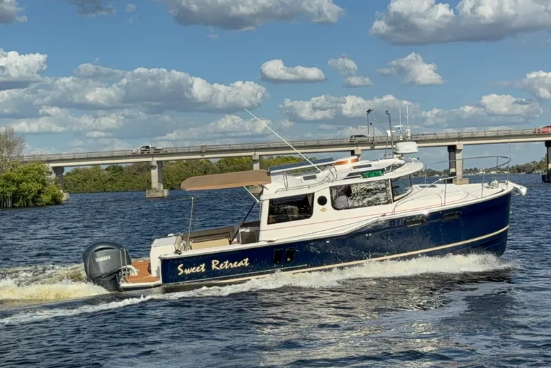 The Image of 2022 Ranger Tugs R-27 boat cruising on a river under a cloudy sky. - 0