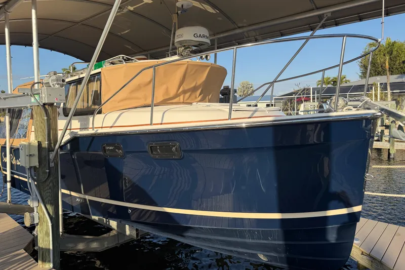Slide: The Image of 2022 Ranger Tugs R-27 boat docked under canopy, featuring sleek blue hull design. - 5