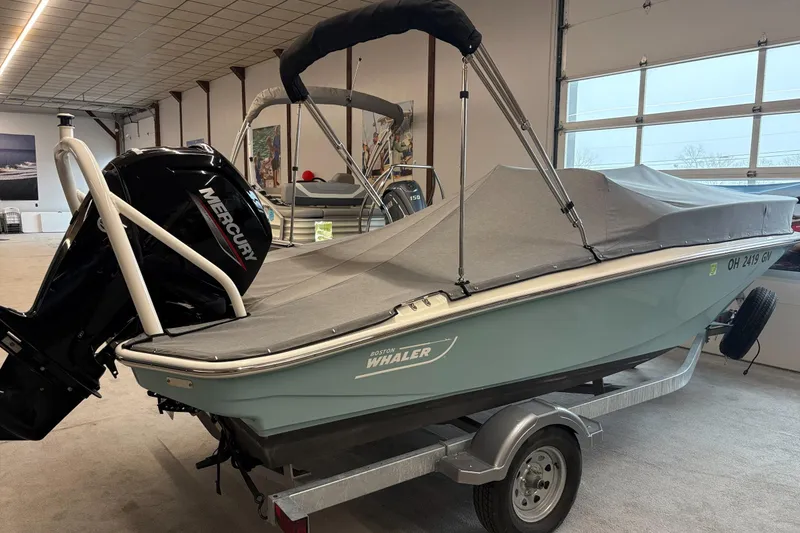 Slide: The Image of 2025 Boston Whaler 160 Super Sport boat with cover and Mercury engine in a showroom. - 2