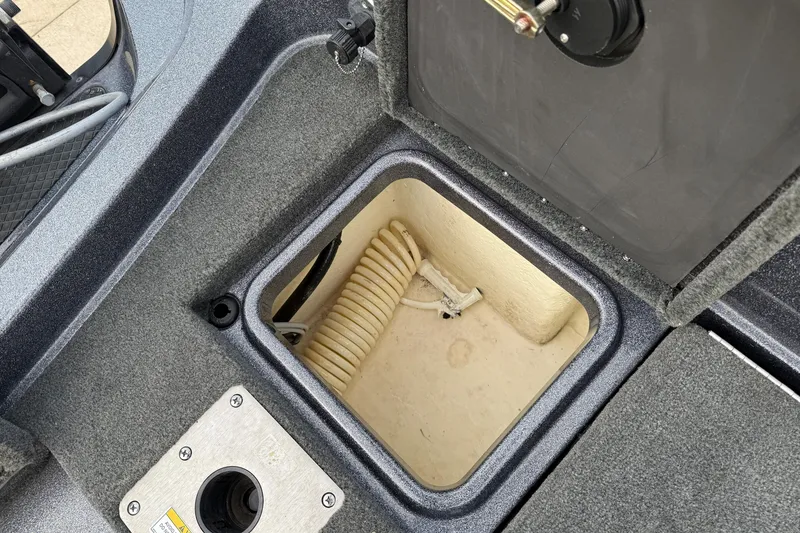 Slide: The Image of Open storage compartment in 2015 Lund 202 Pro-V GL boat, showing coiled hose and wiring. - 32