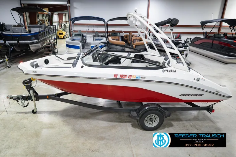 The Image of 2024 Yamaha AR195 boat in showroom, red and white design, on trailer. - 2