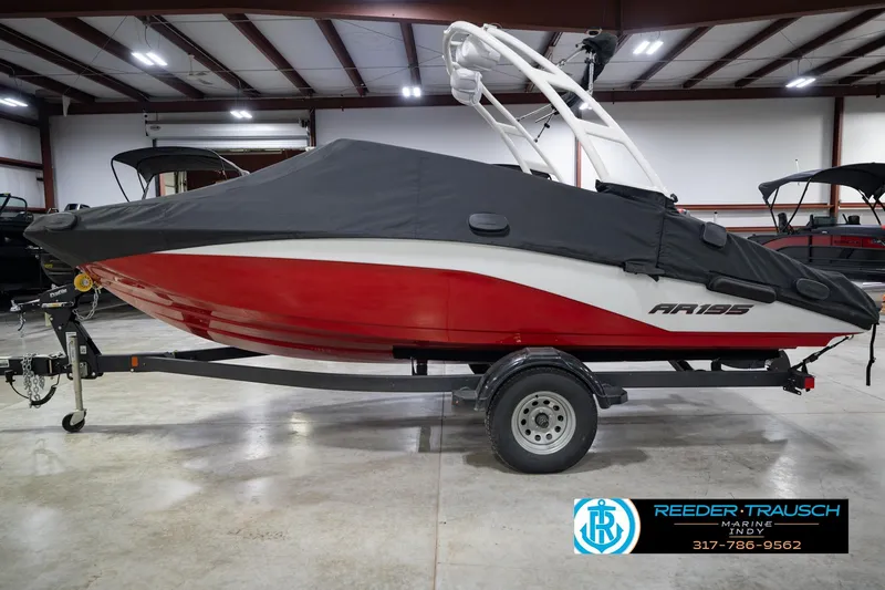 Slide: The Image of 2024 Yamaha Boats AR195, red and white, covered, on trailer in indoor showroom. - 57