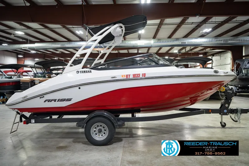 Slide: The Image of 2024 Yamaha Boats AR195 in showroom, red and white design, on trailer. - 7