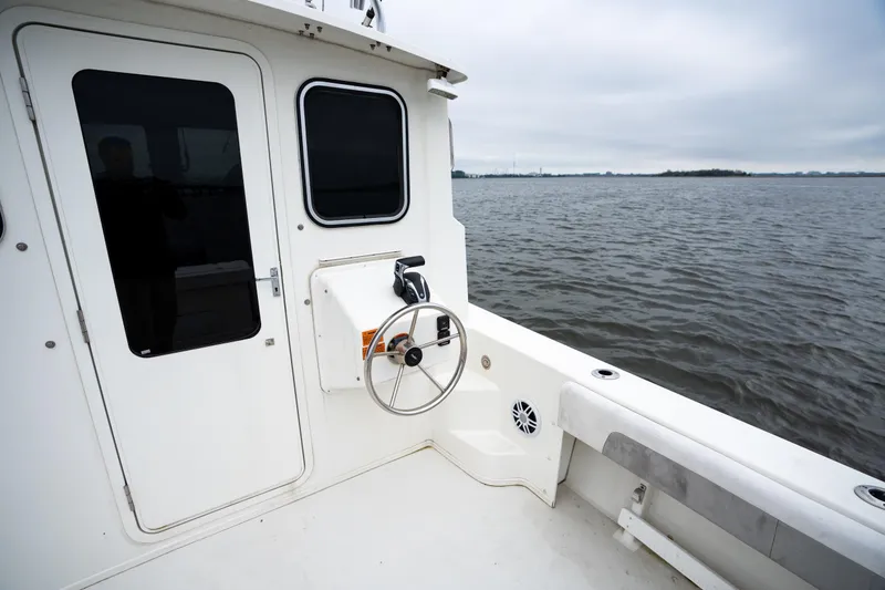 Slide: The Image of 2021 Parker 2520 XLD Sport Cabin boat on calm water, featuring cabin door and steering wheel. - 15