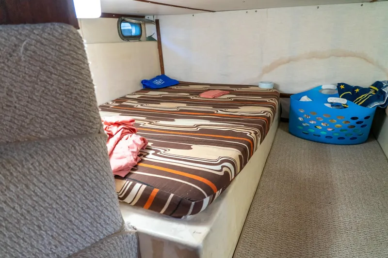 Slide: The Image of 1974 Boatel 47 Islander cabin with striped bedding and laundry basket. - 25