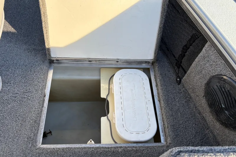 Slide: The Image of 2005 Lund 2025 Pro-V LE boat storage compartment with a white container inside. - 13