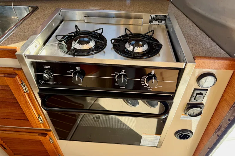 Slide: The Image of 2012 Ranger Tugs R-29 kitchen stove with dual burners and oven, featuring wooden cabinetry. - 14