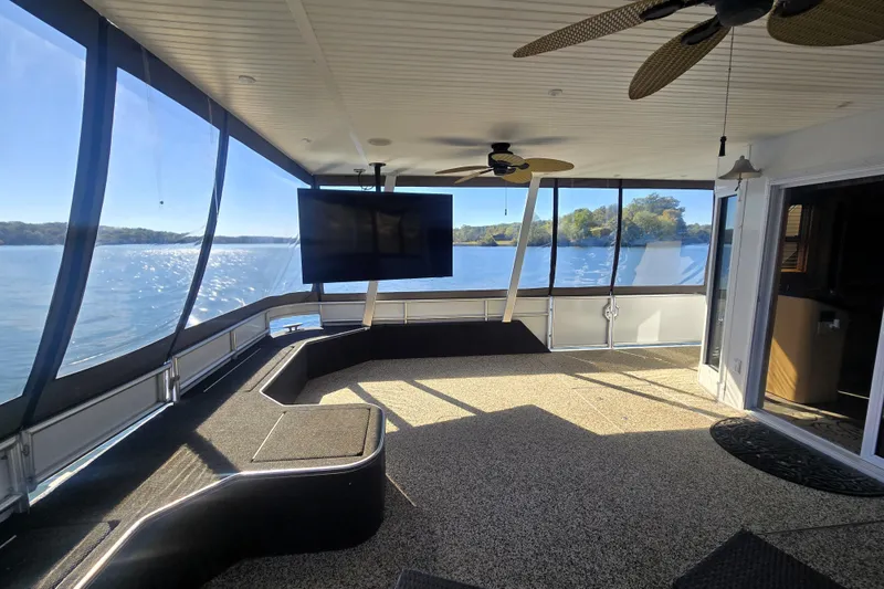 Slide: The Image of Spacious 2013 Thoroughbred houseboat interior with large windows, ceiling fans, and a mounted TV. - 16