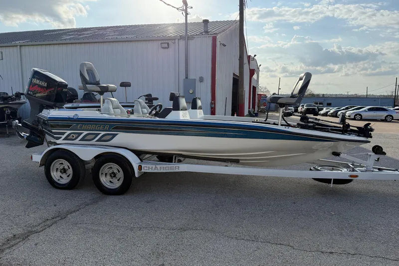 Slide: The Image of 1999 Charger 195TF boat on trailer, parked outside a building under a cloudy sky. - 17
