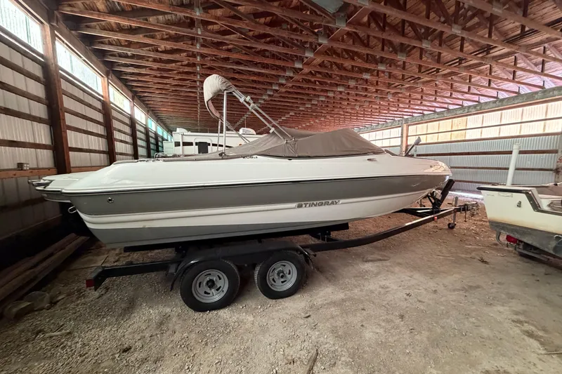 The Image of 2019 Stingray 208 LS boat on trailer in a spacious indoor storage facility. - 0