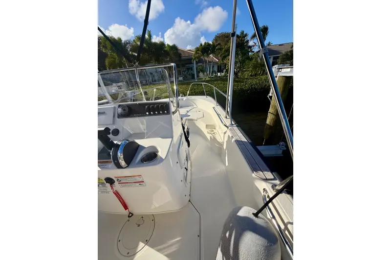 Slide: The Image of 2025 Boston Whaler 170 Montauk boat interior with console and seating, docked near lush greenery. - 10