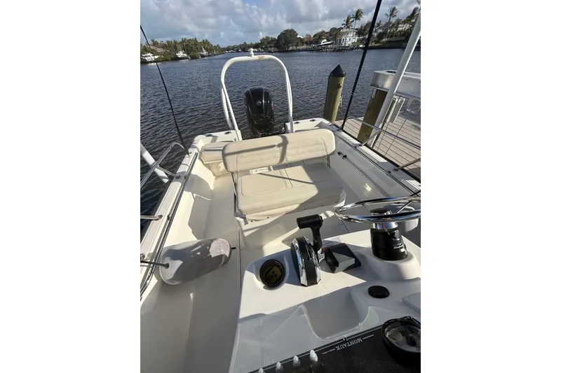 Slide: The Image of 2025 Boston Whaler 170 Montauk boat interior with steering wheel and seating, docked by a scenic river. - 8