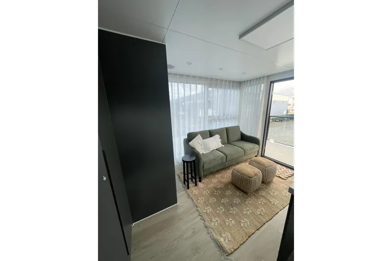 Slide: The Image of Modern houseboat interior with cozy sofa, poufs, and large windows, ALLHOUSE HB-1250, 2025 model. - 14