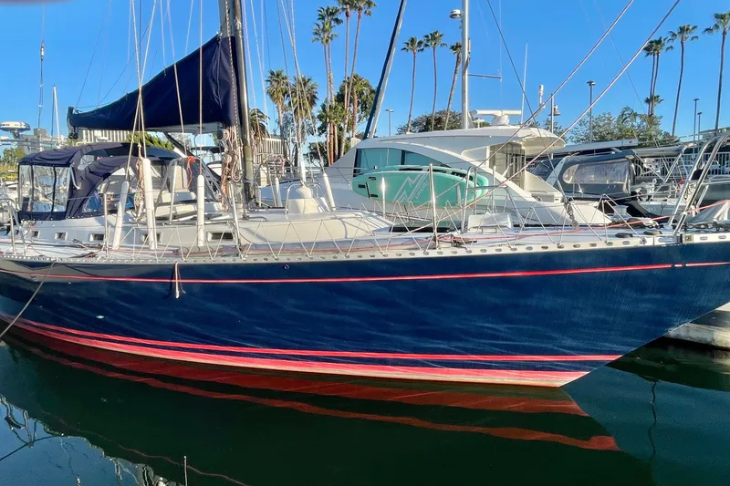 The Image of 1982 Stevens cutter sailboat docked in marina, blue hull with red stripe, clear sky. - 0