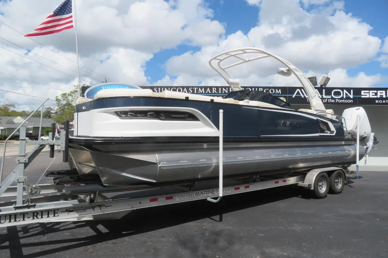 Slide: The Image of 2026 Avalon Excalibur LTD Quad Lounger on trailer, American flag, blue sky. - 12