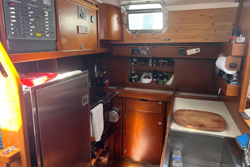 Slide: The Image of Compact kitchen in a 1986 Amel Mango sailboat, featuring wooden cabinetry and essential appliances. - 37