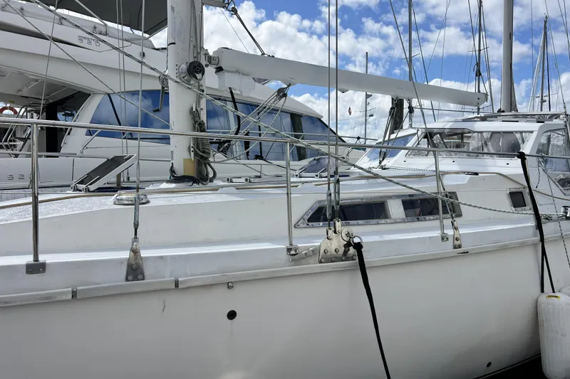 Slide: The Image of 1986 Amel Mango sailboat docked at marina, surrounded by other yachts under a partly cloudy sky. - 50