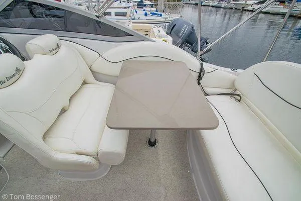 Slide: The Image of 2004 Crownline 250 CR boat interior with white seating and table, docked at marina. - 38