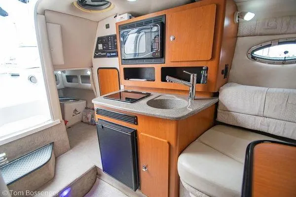 Slide: The Image of 2004 Crownline 250 CR boat interior with kitchenette, featuring sink, microwave, and seating area. - 45