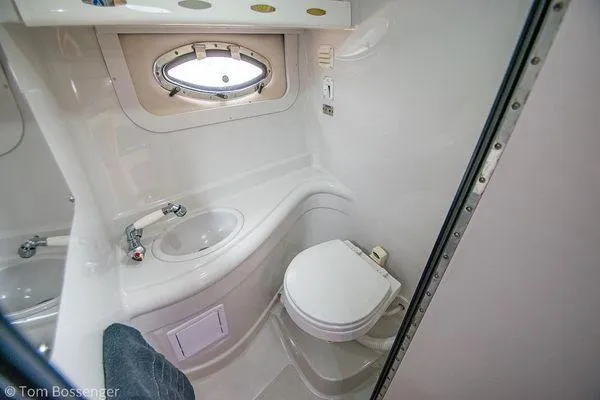 Slide: The Image of 2004 Crownline 250 CR boat bathroom with sink, toilet, and porthole window. - 47