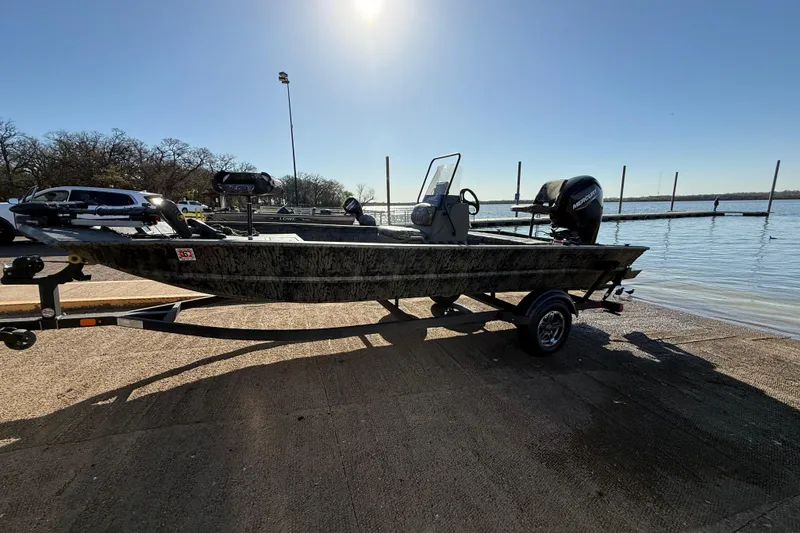 Slide: The Image of 2025 Tracker Grizzly 1860 MVX CC boat on trailer by a lake under clear sky. - 55