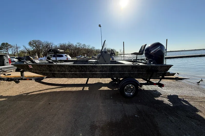Slide: The Image of 2025 Tracker Grizzly 1860 MVX CC boat on trailer by a lake under clear sky. - 56