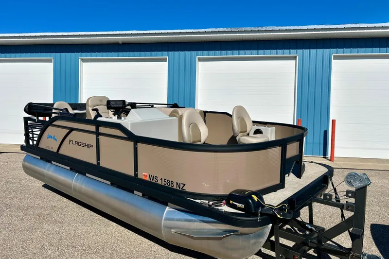 Slide: The Image of 2023 Flagship 200 Lounge Lounger pontoon boat parked near blue garage doors. - 2