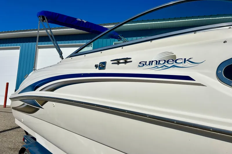 Slide: The Image of 2000 Sea Ray 240 Sundeck boat on trailer, blue cover, parked near blue building. - 6