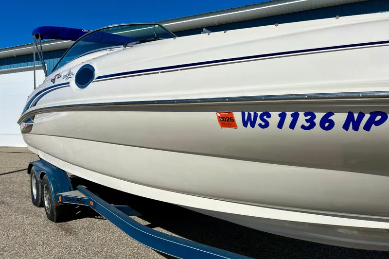 Slide: The Image of 2000 Sea Ray 240 Sundeck boat with blue accents, parked near a blue building. - 7