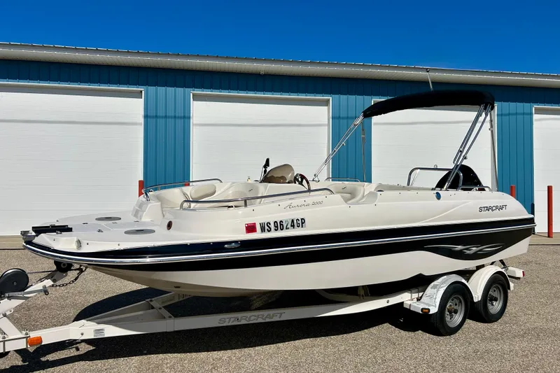 Slide: The Image of 2004 Starcraft Aurora 2000 OB boat on trailer, parked near blue building. - 56